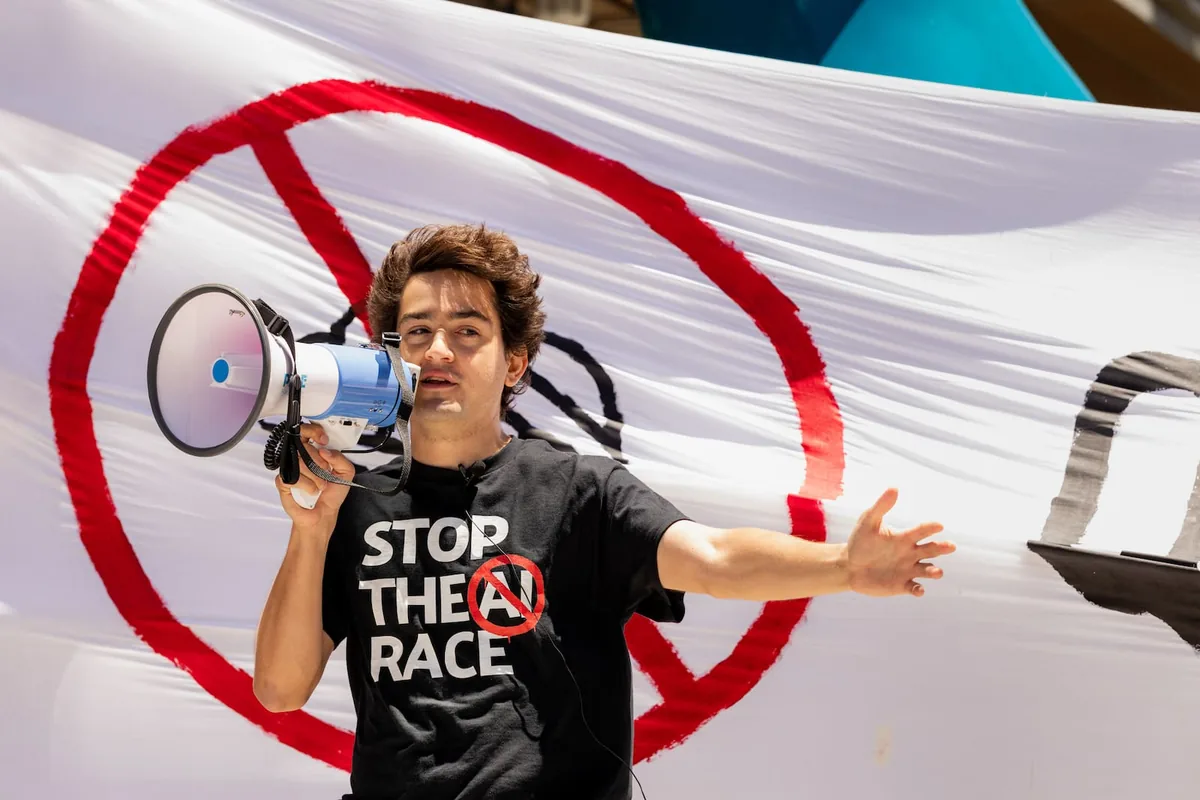 Michaël Trazzi speaks into a megaphone in front of a large crossed-out AI banner